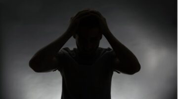 رجل يقف في ظلام مع رأسه بين يديه، يعبر عن مشاعر القلق أو التوتر، خلفية ضبابية.