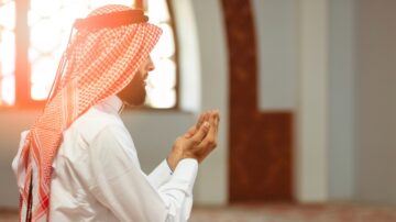 رجل عربي يرتدي شماغًا يتعبد في مسجد، مع ضوء الشمس يضيء من خلفه، يعبر عن الإيمان والتركيز أثناء الصلاة.