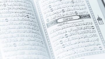 نصوص من القرآن الكريم مكتوبة باللغة العربية، يظهر فيها الخط العربي التقليدي مع تمييز لبعض الآيات. الكتاب مفتوح على صفحة تحتوي على سورة معينة، مما يبرز جمال التصميم والتنسيق.