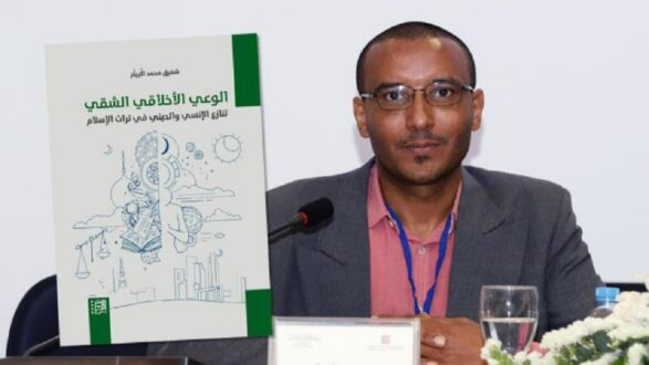 رجل يبتسم ويجلس أمام طاولة في مؤتمر، يحمل كتاب بعنوان "الوعي الأنتلوجي الشفهي: تاريخ الإسلام والعلم في بلاد الإسلام" خلفه، مع رسومات توضيحية للكتاب تظهر عناصر ثقافية.