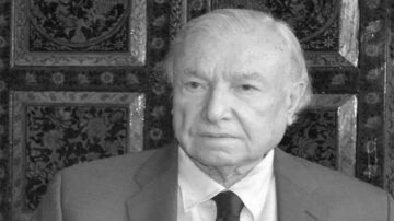 رجل مسن يرتدي بدلة رسمية وقميص مع ربطة عنق، يظهر بملامح جدية في خلفية مزخرفة.