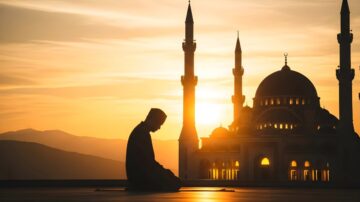 Silhouette of a person praying at sunset in front of a mosque with tall minarets. The warm glow of the sun sets behind the architectural features, creating a serene and peaceful atmosphere.