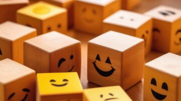 مكعبات خشبية ملونة تحمل وجوه تعبيرية مبتسمة، تتوزع على سطح خشبي. تعكس الألوان الزاهية والرسوم التعبيرية أجواء من المرح والإيجابية.