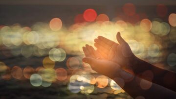 أيدٍ ممدودة نحو الضوء مع خلفية مشوشة تعكس ألوانًا دافئة تعبر عن الأمل والتواصل الروحي.