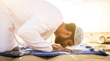 رجل يؤدي الصلاة في الصحراء على سجادة صلاة مع غروب الشمس، يرتدي ملابس تقليدية وعقال، يعبّر عن الخشوع والسكينة.