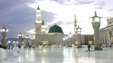 Mosquée du Prophète à Médine, avec sa coupole verte et ses minarets majestueux, entourée de visiteurs en pèlerinage. Le ciel crépusculaire ajoute une ambiance apaisante à l'architecture islamique.