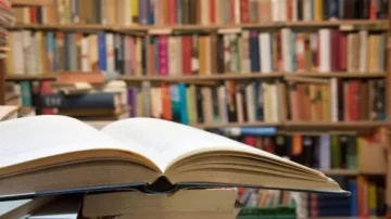 Livre ouvert au premier plan avec une bibliothèque bien fournie en arrière-plan, présentant une vaste collection de livres. Scène idéale pour les amateurs de lecture et de littérature.