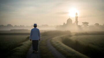 A person in traditional attire walks on a misty path towards a mosque at sunrise, symbolizing the journey of how to live a good life.