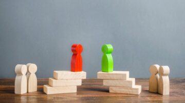 شخصيتان خشبيتان ملونتان باللون الأحمر والأخضر تقفان على درج خشبي، مع وجود شخصيتين أخريين على الدرج أدنى. تعكس الصورة مفهوم التنافس والتفوق.