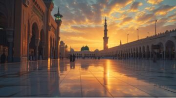 غروب الشمس فوق المسجد النبوي في المدينة المنورة، يظهر الأضواء المتلألئة على الأرضية الرخامية. المآذن والقبة الخضراء تبرز في الخلفية، مع سماء ملونة بالسحب.