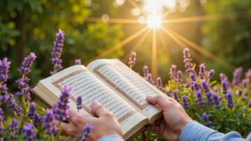 كتاب الله مفتوح في حديقة مزهرة، بأيدي شخص. يضيء أشعة الشمس من خلف الأزهار اللافندر، مما يخلق أجواءً هادئة وروحانية.