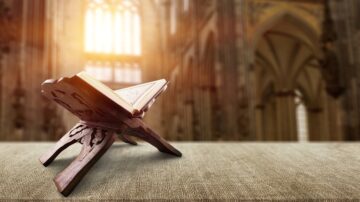 كتاب مفتوح على حامل خشبي في كنيسة، مع خلفية معمارية رائعة وأشعة الشمس تتسلل من النوافذ.