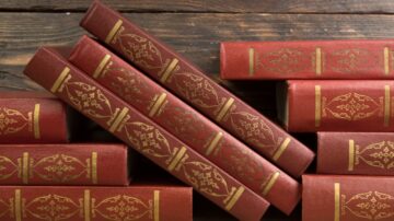 كتب جلدية حمراء متراصة مع تصميم ذهبي، موضوعة على سطح خشبي داكن ترمز إلى كتب التراث في علوم الفقه وتجديده.