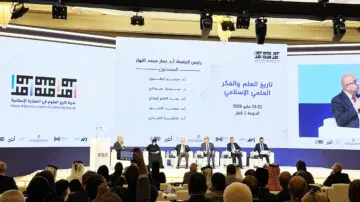 تظهر الصورة جلسة نقاش في ندوة تاريخ العلم والفكر العلمي الإسلامي، المنعقدة في قطر في مايو 2026. يتواجد خمسة متحدثين على المنصة، يتحدثون أمام جمهور في قاعة مؤتمرات حديثة. تشمل الموضوعات المطروحة تاريخ العلم وتأثيره في الحضارة الإسلامية.
