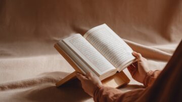 Open Quran on a wooden stand with hands gently holding the pages, symbolizing a believer responding to Allah and His Messenger in absolute submission.