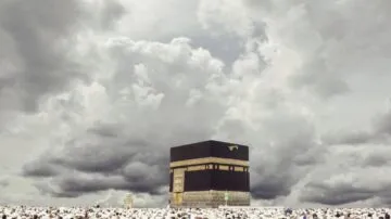 صورة توضح الكعبة المشرفة محاطة بحشود من الحجاج يرتدون الملابس البيضاء، تحت سماء غائمة. تُظهر الصورة أهمية الكعبة كمركز للعبادة في الإسلام.