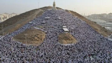 مئات الآلاف من الحجاج يرتدون ملابس الإحرام خلال فريضة الحج في مكة، مع جبل عرفات في الخلفية ومئذنة تضيء المنطقة.