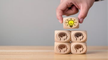 صورة تظهر يدًا تضع مكعبًا خشبيًا به رمز لمبة فوق أربعة مكعبات خشبية تحمل رسومات لأدمغة. تعبر الصورة عن مفهوم الإبداع والتفكير.