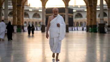 رجل مسن يرتدي الإحرام يسير في صحن المسجد الحرام بمكة المكرمة، مع أضواء المساء في الخلفية. تعكس الصورة روح السعي بين الصفا والمروة، والحج، والعبادة.