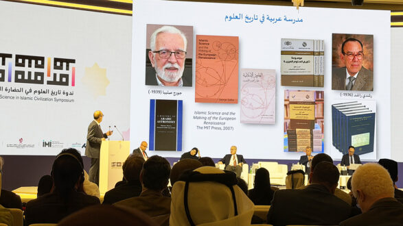 صورة من ندوة حول تاريخ العلوم الإسلامية، تظهر متحدثًا يقدم عرضًا على الشاشة خلفه. يتضمن العرض كتبًا تتعلق بالعلوم الإسلامية وتاريخها، بالإضافة إلى صور لمؤلفين بارزين. الجمهور يتكون من رجال ونساء يجلسون في قاعة مؤتمرات.