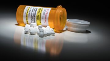 An orange prescription bottle tipped over with white pills scattered on a dark surface, representing the medical and emotional challenges faced when overcoming addiction.