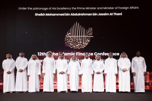 صورة جماعية لمؤتمر التمويل الإسلامي الثاني عشر، مع عدد من الشخصيات البارزة في الصف الأمامي. يظهر في الخلفية شعار المؤتمر مع تفاصيل حول رعاية رئيس الوزراء ووزير الخارجية. يجسد الحدث التركيز على التعاون في مجال التمويل الإسلامي.