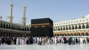 Vue de la Kaaba au sein de la Mosquée al-Haram à La Mecque, entourée de pèlerins en procession. Les minarets se dressent en arrière-plan sous un ciel clair. L'ambiance révèle l'importance spirituelle du lieu pour les musulmans.