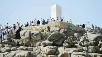 Des milliers de pèlerins en vêtements traditionnels se rassemblent sur une colline rocheuse, près d'un monument blanc, lors d'un pèlerinage. Le paysage aride et les rochers environnants soulignent l'importance spirituelle du site.