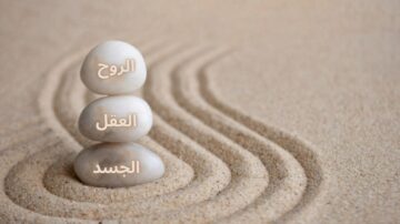 صورة توضح ثلاثة أحجار بيضاء مرتبة فوق بعضها البعض على رمال ناعمة، مع نصوص تشير إلى الروح، العقل، والجسد. التصميم يعكس مفهوم التوازن والهدوء.