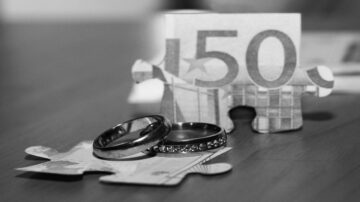 خواتم زفاف معدنية تتواجد على قطع من الألغاز الورقية، مع ورقة نقدية من فئة 150 يورو في الخلفية. تعكس الصورة موضوع الحب والاستقرار المالي.