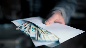 يد تحمل ظرفًا مفتوحًا يحتوي على نقود ورقية من فئة 20 يورو، مما يشير إلى عملية تبادل مالي أو هدية.