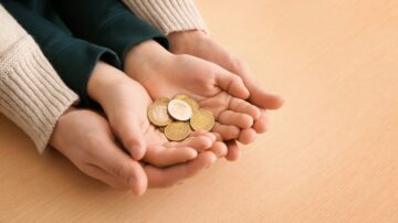 أيدٍ صغيرة تحمل عملات معدنية متنوعة على سطح خشبي. تظهر الأيدي المتشابكة بشكل يشير إلى التعاون والكرم، مما يعكس أهمية المال في العلاقات الإنسانية والمشاركة.