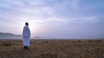 Person in traditional white attire standing in a desert landscape at dawn during the 10 days of Dhul Hijjah, facing a soft sunrise with misty mountains in the background, evoking peace and reflection.
