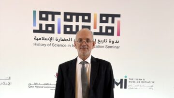رجل مسن يرتدي بدلة رسمية يقف أمام خلفية تحمل شعارات ندوة تاريخ العلوم في الحضارة الإسلامية ومبادرة الإسلام والمسلمين.