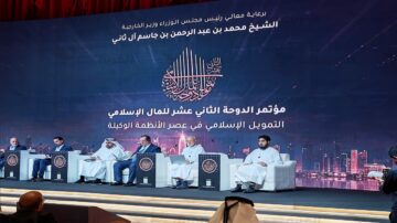 مؤتمر الدوحة الثاني عشر للتمويل الإسلامي، يتضمن خمسة متحدثين على منصة، مع خلفية تحمل شعار المؤتمر وأفق مدينة حديثة. يتحدث المشاركون عن التطورات في الأنظمة المالية الإسلامية.