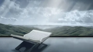 Livre ouvert sur un support, avec des collines verdoyantes et un ciel nuageux en arrière-plan, créant une atmosphère paisible et inspirante.