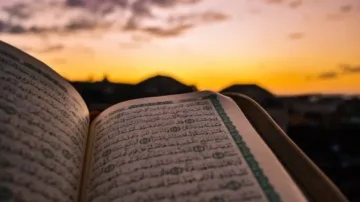 Livre ouvert du Coran en premier plan, avec un coucher de soleil en arrière-plan. Les pages sont ornées d'écritures arabes sur fond de paysages. Ambiance paisible et spirituelle.