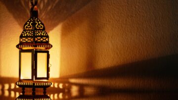 Decorative lantern casting intricate shadows on a wall, illuminated softly from within to highlight its ornate design, capturing the tranquil and respectful atmosphere of interfaith dialogue in Islam