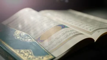Livre sacré ouvert avec des pages ornées de calligraphie arabe, lumière douce mettant en valeur les détails du texte et de la couverture décorative.