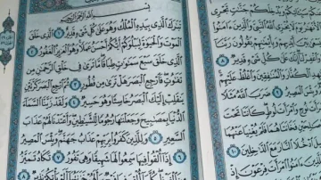 Texte calligraphié en arabe du Coran sur des pages ornées, présentant des versets religieux avec des motifs décoratifs en bleu et doré.