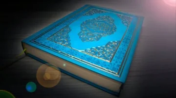 Livre sacré ouvert sur une table, couverture bleue ornée de motifs dorés. Lumière douce illuminant l'image, créant une ambiance spirituelle et contemplative.