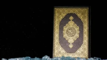 Livre du Coran présenté sur un fond sombre avec des éléments décoratifs dorés sur la couverture. Des cristaux bleus sont visibles au premier plan, ajoutant une touche artistique à la composition.