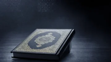 Livre sacré du Coran posé sur une surface en bois sombre, avec un éclairage doux et une ambiance mystique. Détails dorés sur la couverture illustrent l'importance spirituelle du texte.