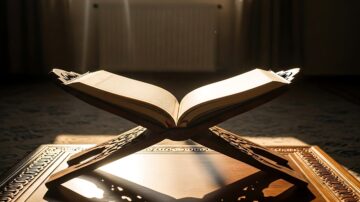 كتاب مفتوح على حامل خشبي، مع أشعة الضوء تتسلل من الخلف، مما يبرز تفاصيل الصفحات. الخلفية غير واضحة، مما يضيف جوًا هادئًا.