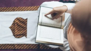 Femme lisant un livre religieux, pointant une page, assise sur un tapis de prière. Ambiance calme et spirituelle, mettant en avant la pratique de la lecture sacrée.