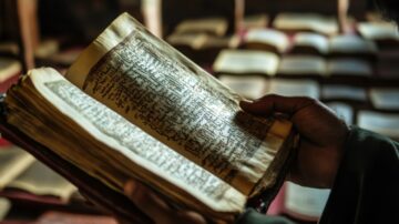 كتاب قديم يُظهر نصوصًا مكتوبة بخط يدٍ تناقش المسألة الاجتهادية، يُمسك به شخص في بيئة مظلمة مع خلفية تحتوي على كتب أخرى