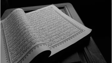 Livre ouvert avec des pages écrites en calligraphie arabe sur un fond sombre, mettant en avant des versets du Coran. L'image illustre la beauté de la littérature islamique et la tradition de la lecture sacrée.