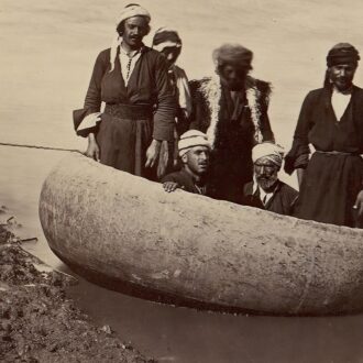 مجموعة من الرجال والنساء يرتدون ملابس تقليدية يقفون حول قارب مصنوع من مادة طبيعية. يظهرون في وضعية تفاعلية، حيث يبتسم بعضهم بينما يبدو آخرون جادين. البيئة المحيطة تحتوي على مياه هادئة، مما يعكس مشهدًا ثقافيًا تاريخيًا.