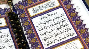 Page d'un livre sacré avec des calligraphies arabes, incluant des versets et des motifs décoratifs colorés. Un chapelet noir est posé à côté, ajoutant un élément de spiritualité.