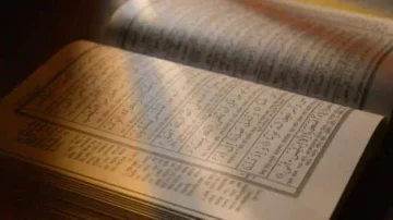Livre ouvert avec des pages écrites en arabe, présentant un texte manuscrit et des colonnes bien organisées, illuminé par une lumière douce, créant une ambiance calme et studieuse.